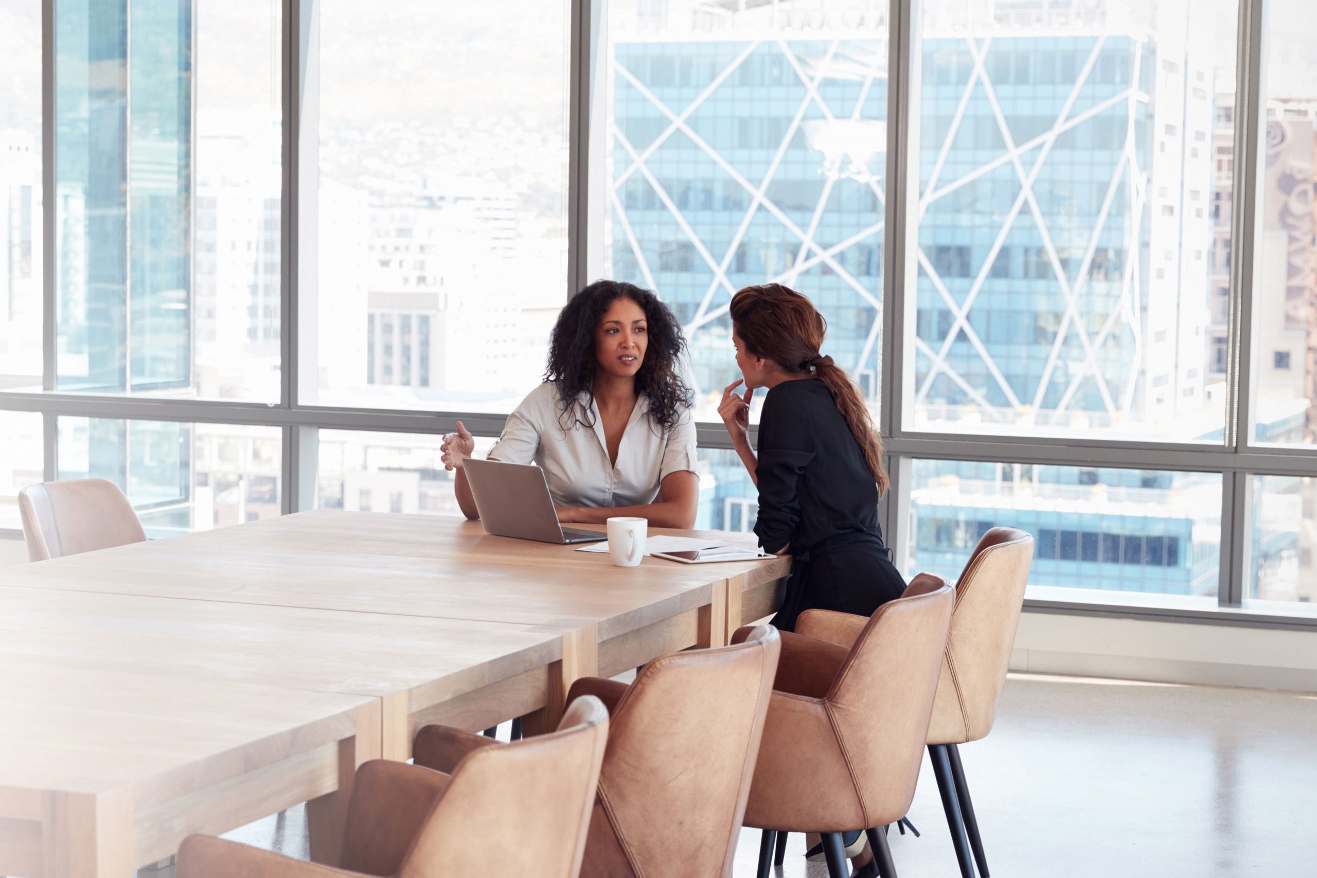 Two women sitting at a table in front of a laptop.